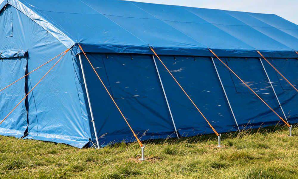 Emergency frame tent secured with thick guy ropes and steel ground stakes in windy field conditions Emergency frame tent secured with thick guy ropes and steel ground stakes in windy field conditions