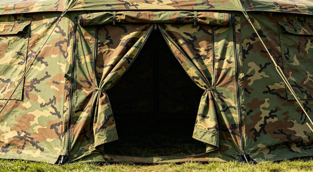 Military tent entrance with double door flaps and zipper detail, woodland camouflage pattern, grassy ground, professional product detail photography professional high quality realistic photography with detailed composition and natural lighting conditions