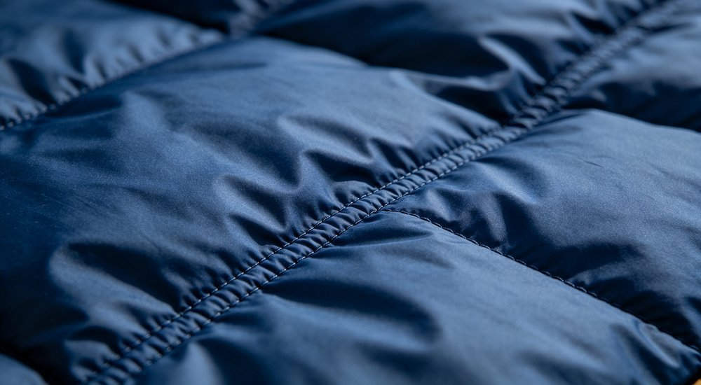 Closeup sleeping bag fabric texture showing polyester material and diamond stitching pattern in navy blue macro detail photography with soft directional lighting for product quality inspection
