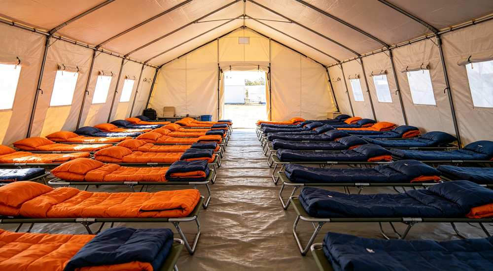 Disaster relief camp at sunset with rows of tents and orange sleeping bags for emergency accommodation deployment photography and humanitarian aid documentation professional