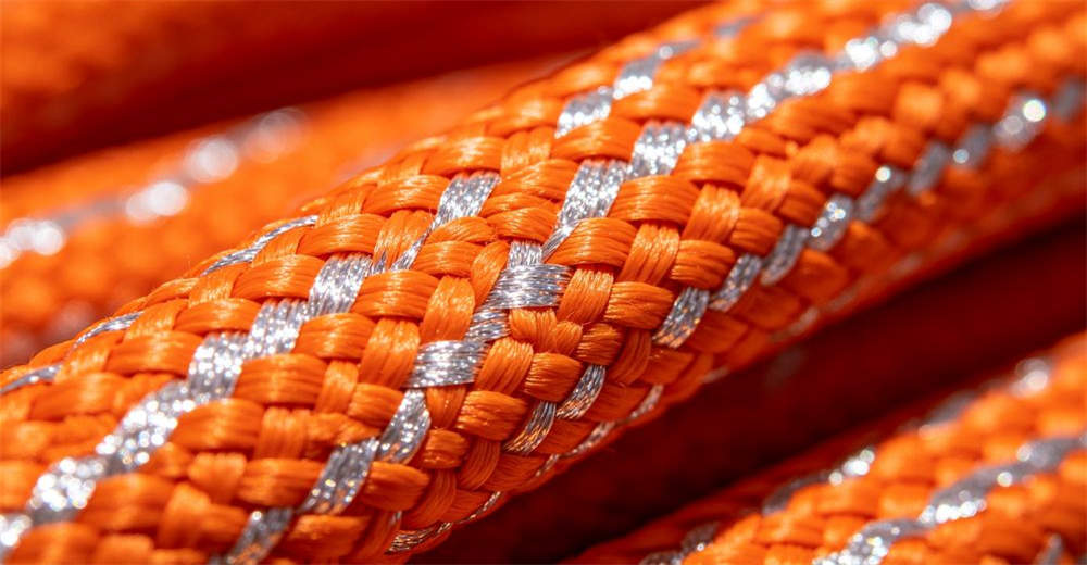Extreme close-up of reflective tape strip woven into orange flood rescue rope outer cover showing luminous yarn and braided pattern for reliable water rescue operations and emergency response