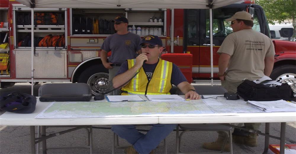 Wide view of emergency operations command center with responders at tables using radios and maps