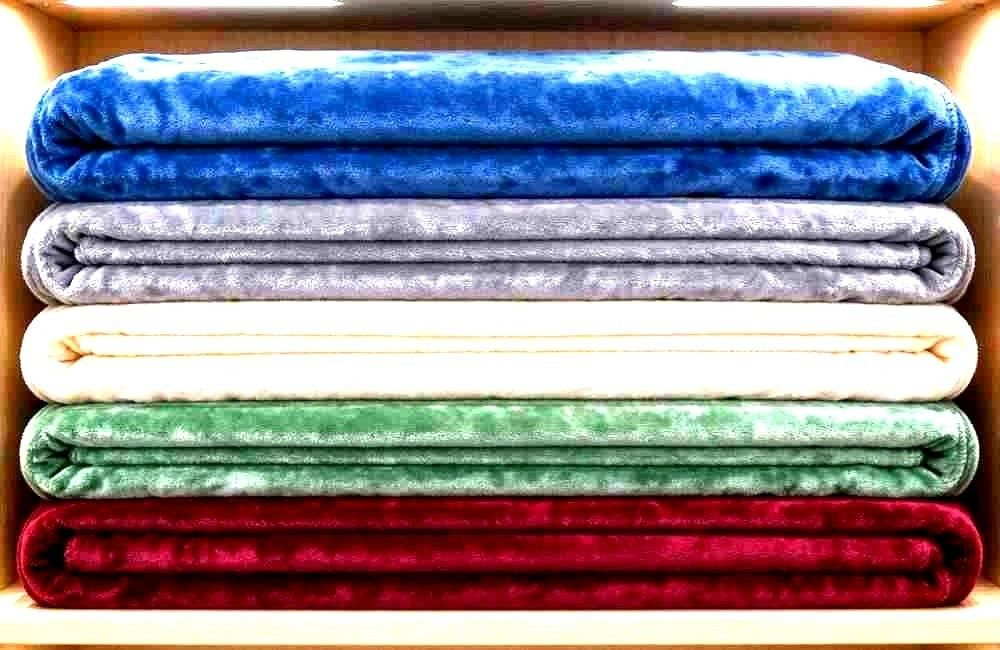 Colorful woven shelter blankets stacked in a relief warehouse, showing refugee blankets wholesale stock in different colors and sizes for bulk orders